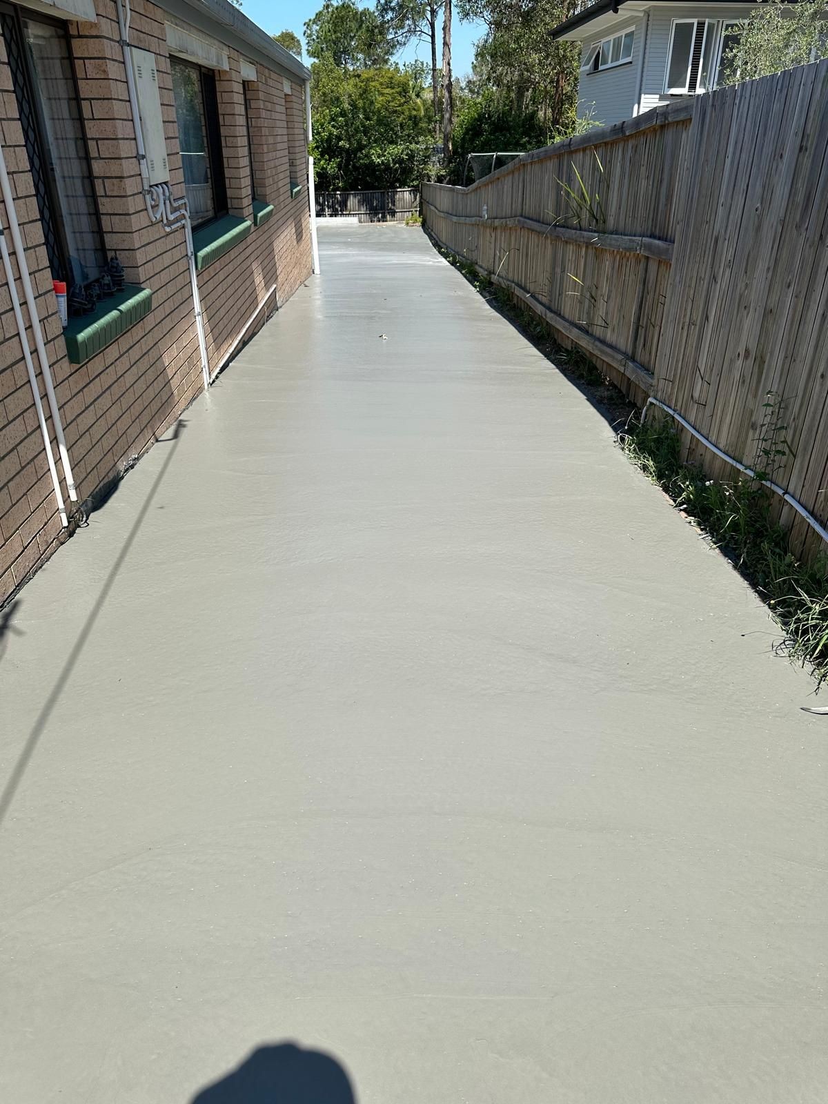 Freshly poured concrete pathway alongside a brick building and wooden fence.