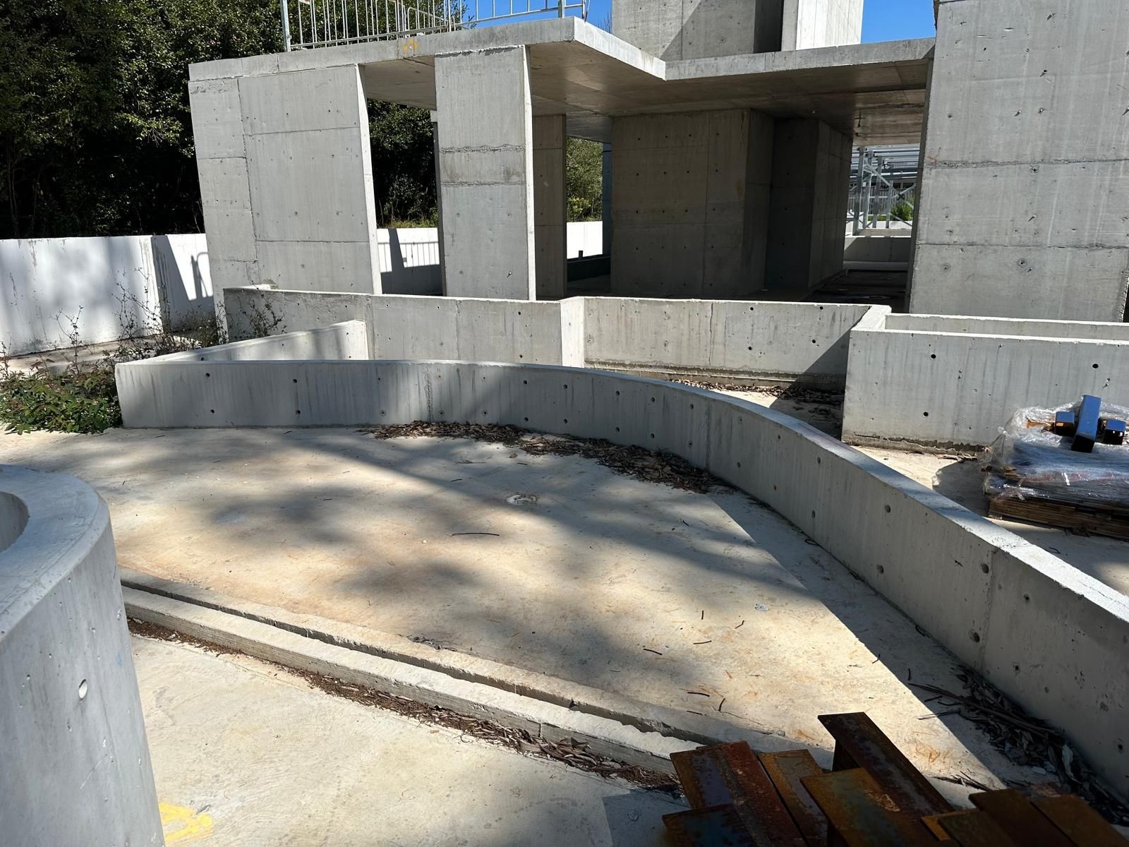 Outdoor view of partially constructed concrete building with curved walls, surrounded by nature.