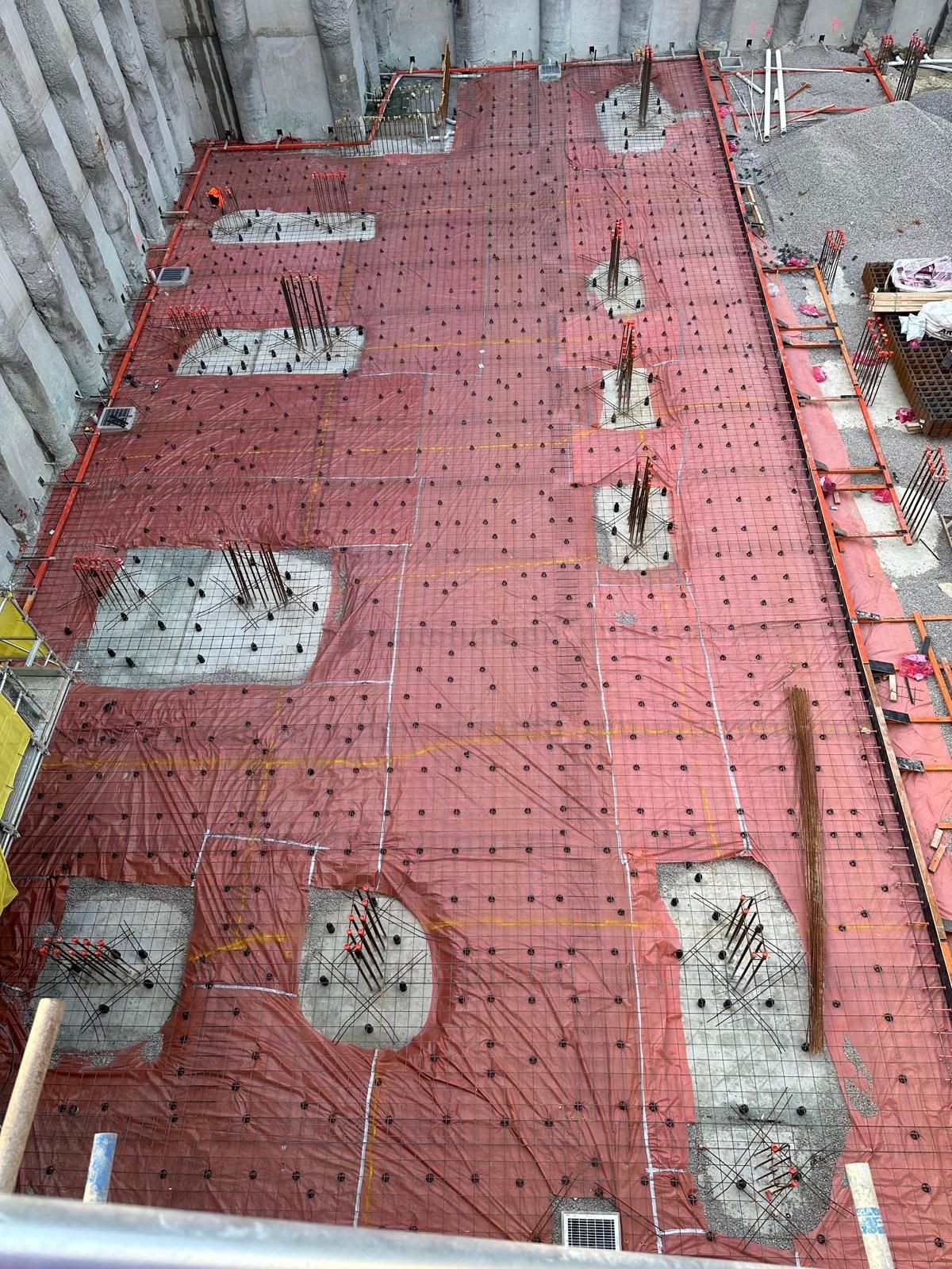 Construction site with rebar and red protective sheeting covering future foundation areas.