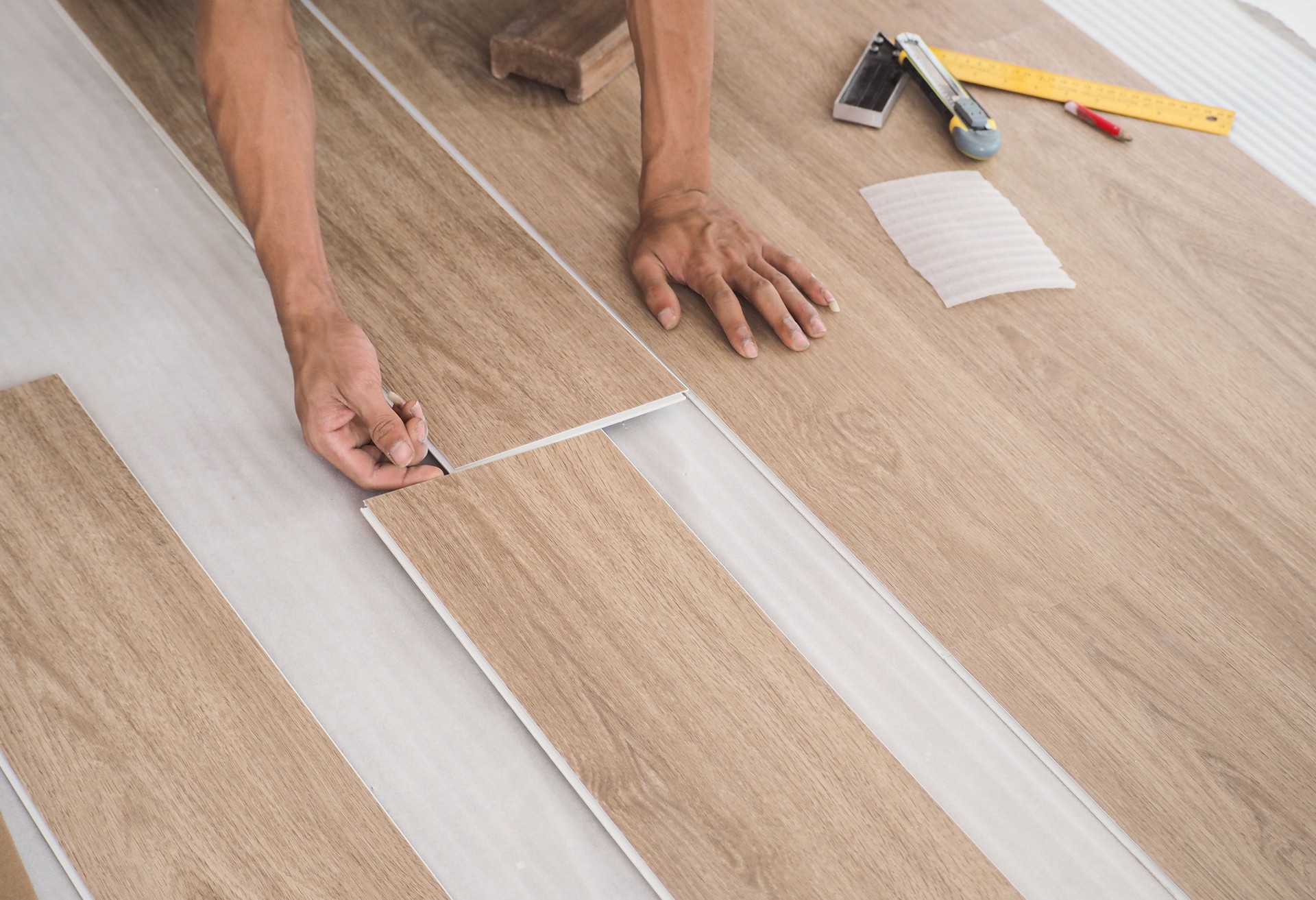 A technician is cutting luxury vinyl floor tiles with a cutter to lay the floor before placing it on the leveling foam.